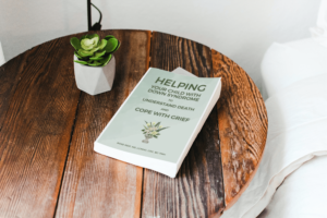 The book 'Helping Your Child with Down syndrome to Understand Death and Cope with Grief' by Rose Reif on a bedside table with a small succulent plant